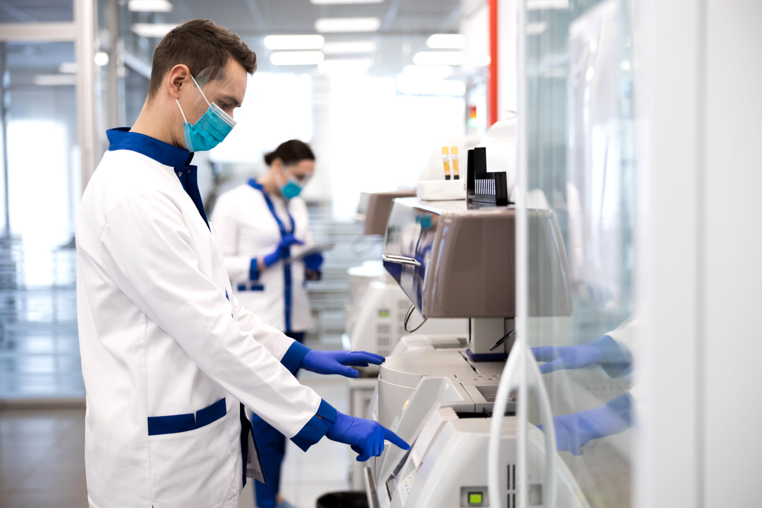 Male researcher in protective medical mask using immunoassay analyzer