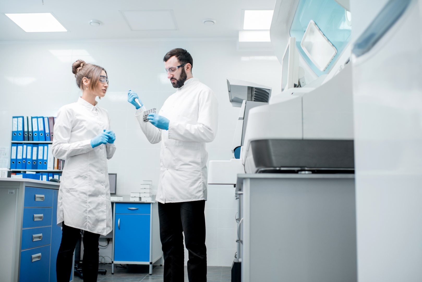 Two lab workers standing in a laboratory. The one on the right is holding equipment in his hands.