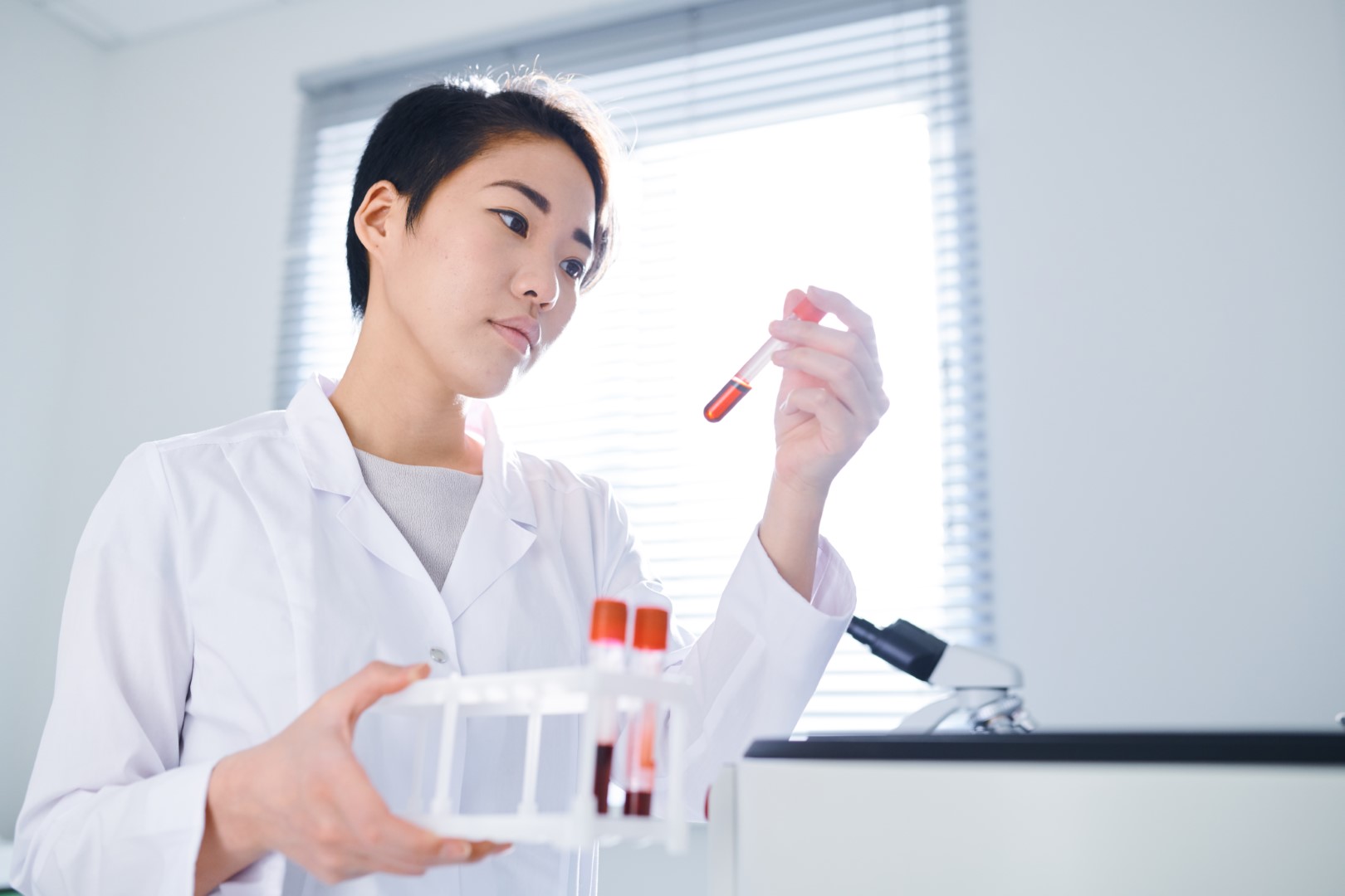 A woman with short hair looking at a vial of blood in her hand.
